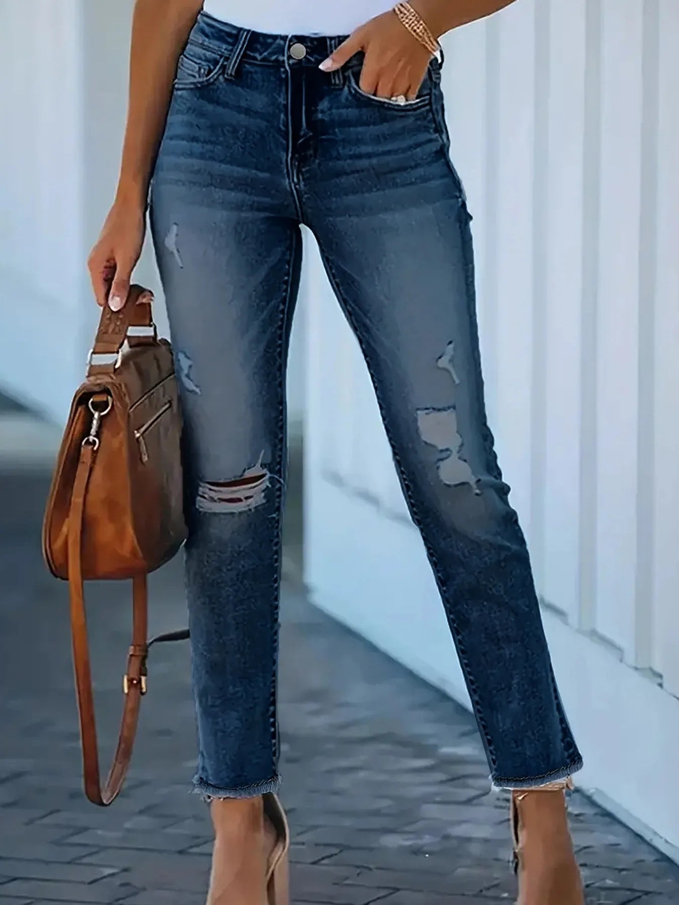 Person wearing distressed blue jeans holding a brown leather handbag.