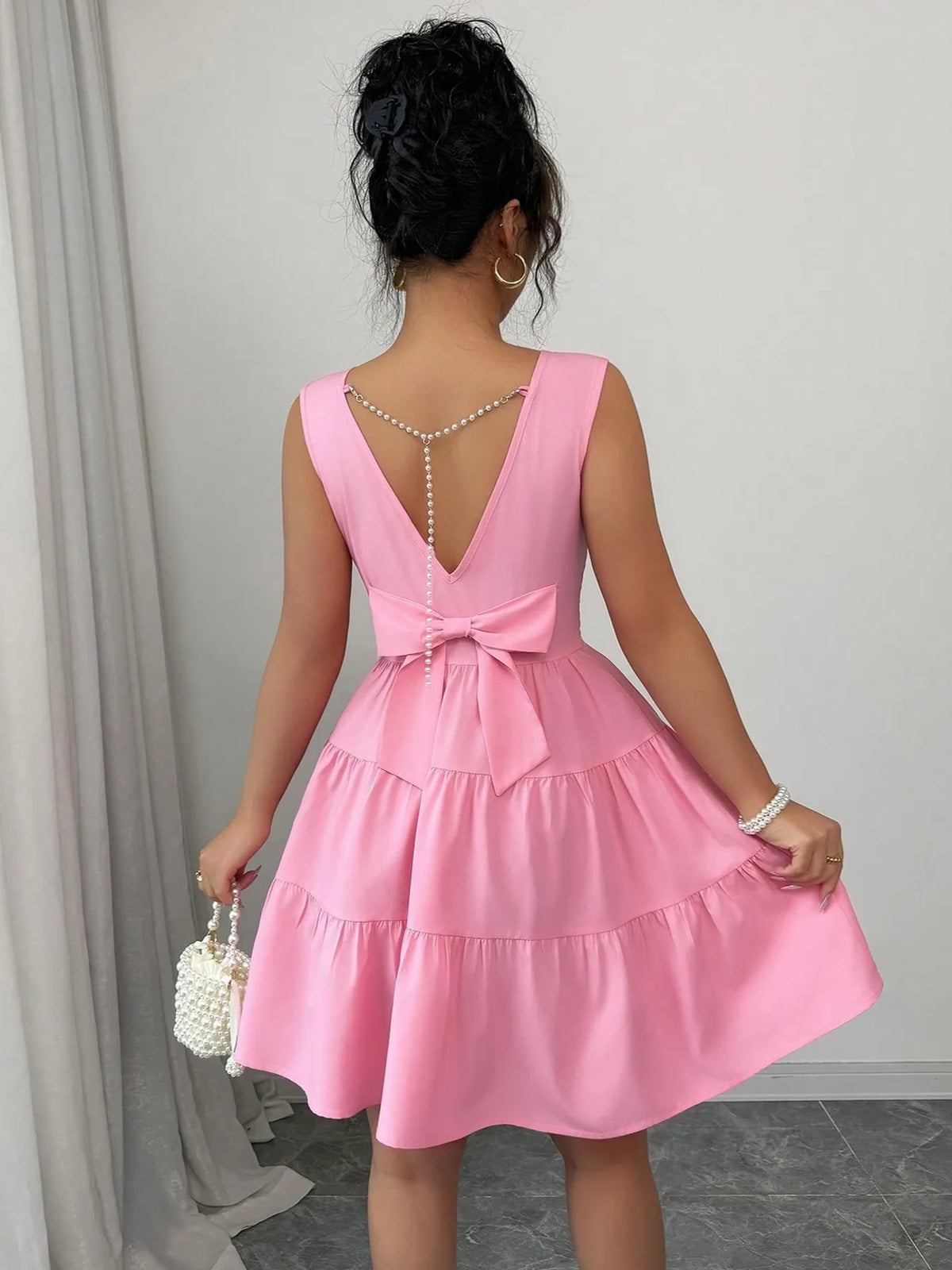 Woman wearing a pink dress with a bow detail in a neutral setting