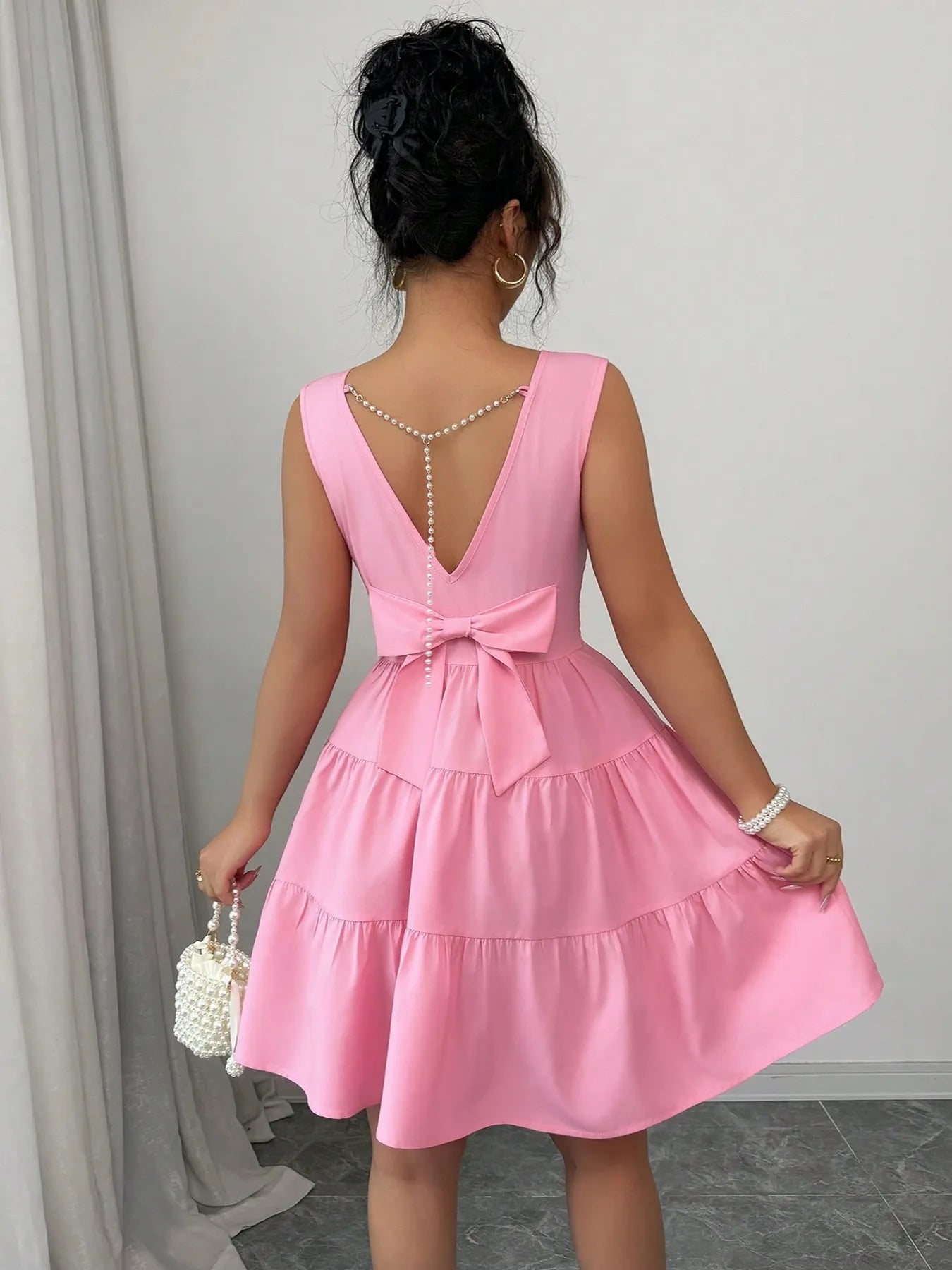 Woman wearing a pink dress with a bow detail in a neutral setting