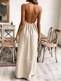 Woman wearing a long, open-back dress in a room with wooden chairs and a mirror.