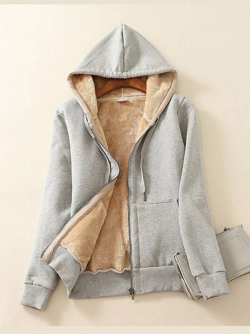 A light gray zip-up hoodie with a plush tan fleece lining, shown open on a hanger against a warm beige background.