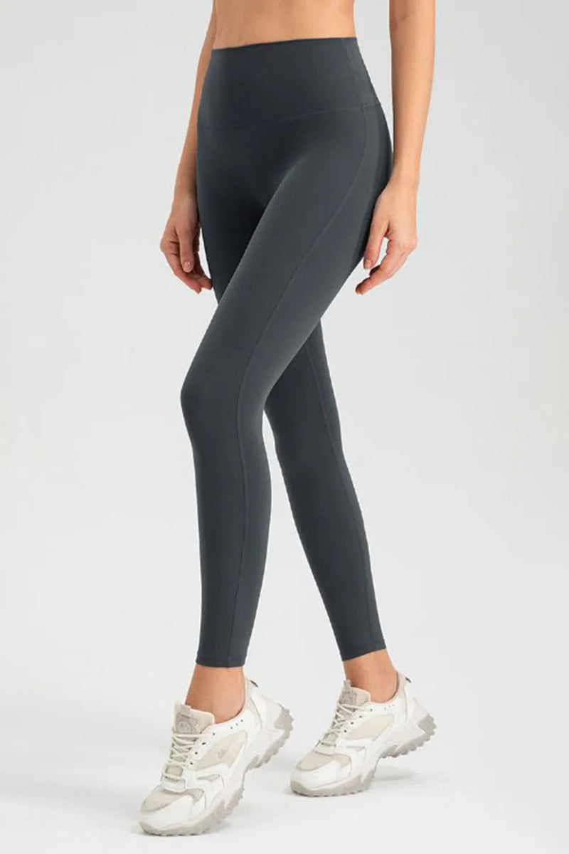 Person wearing dark gray leggings and white sneakers on a light gray background