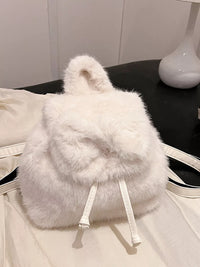 White fluffy backpack on a black surface with a white background