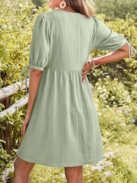 Person wearing a green dress standing in a natural setting with greenery and flowers.