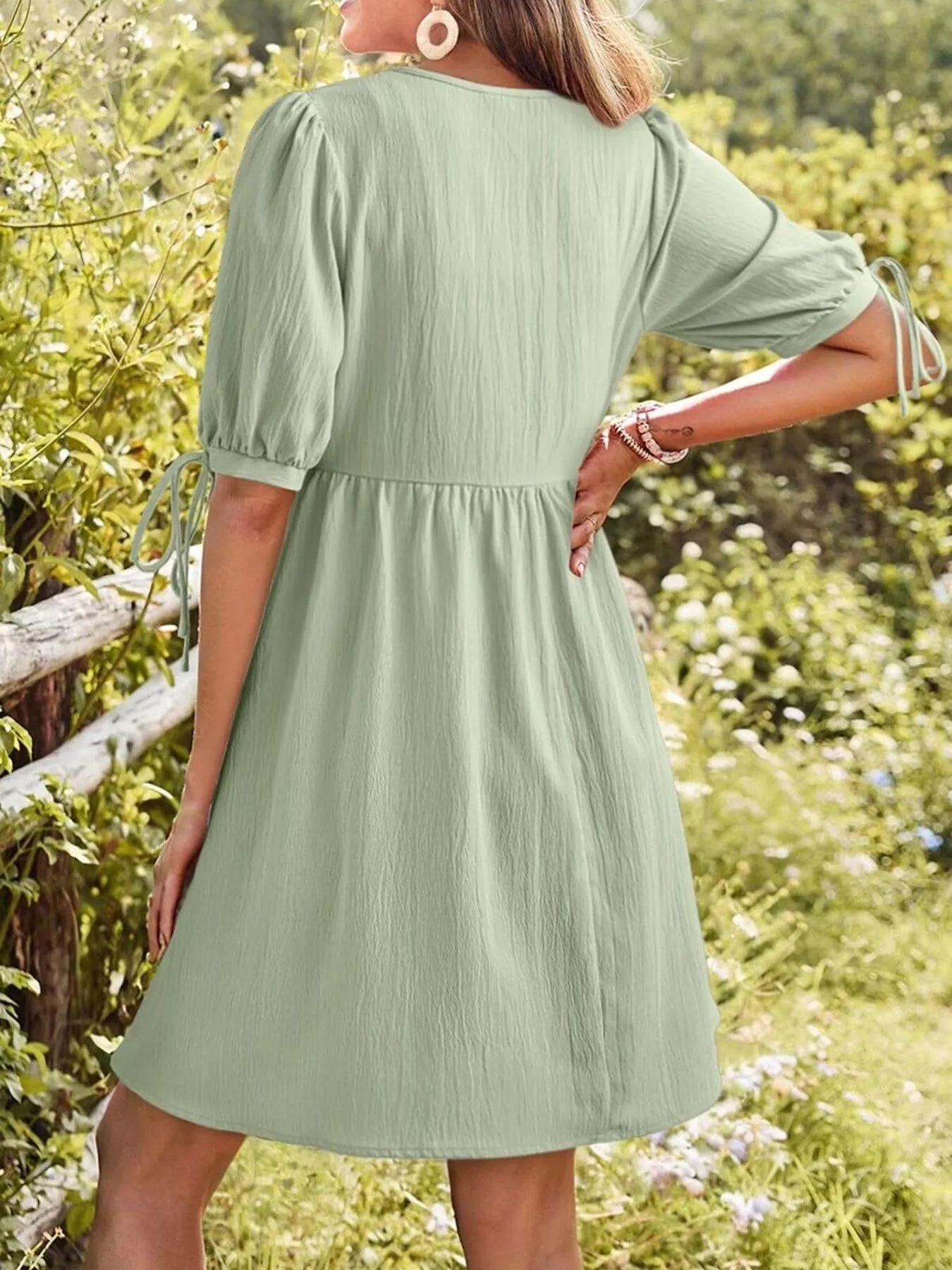 Person wearing a green dress standing in a natural setting with greenery and flowers.