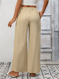Person wearing beige wide-leg pants with a white top against a light wooden panel background.