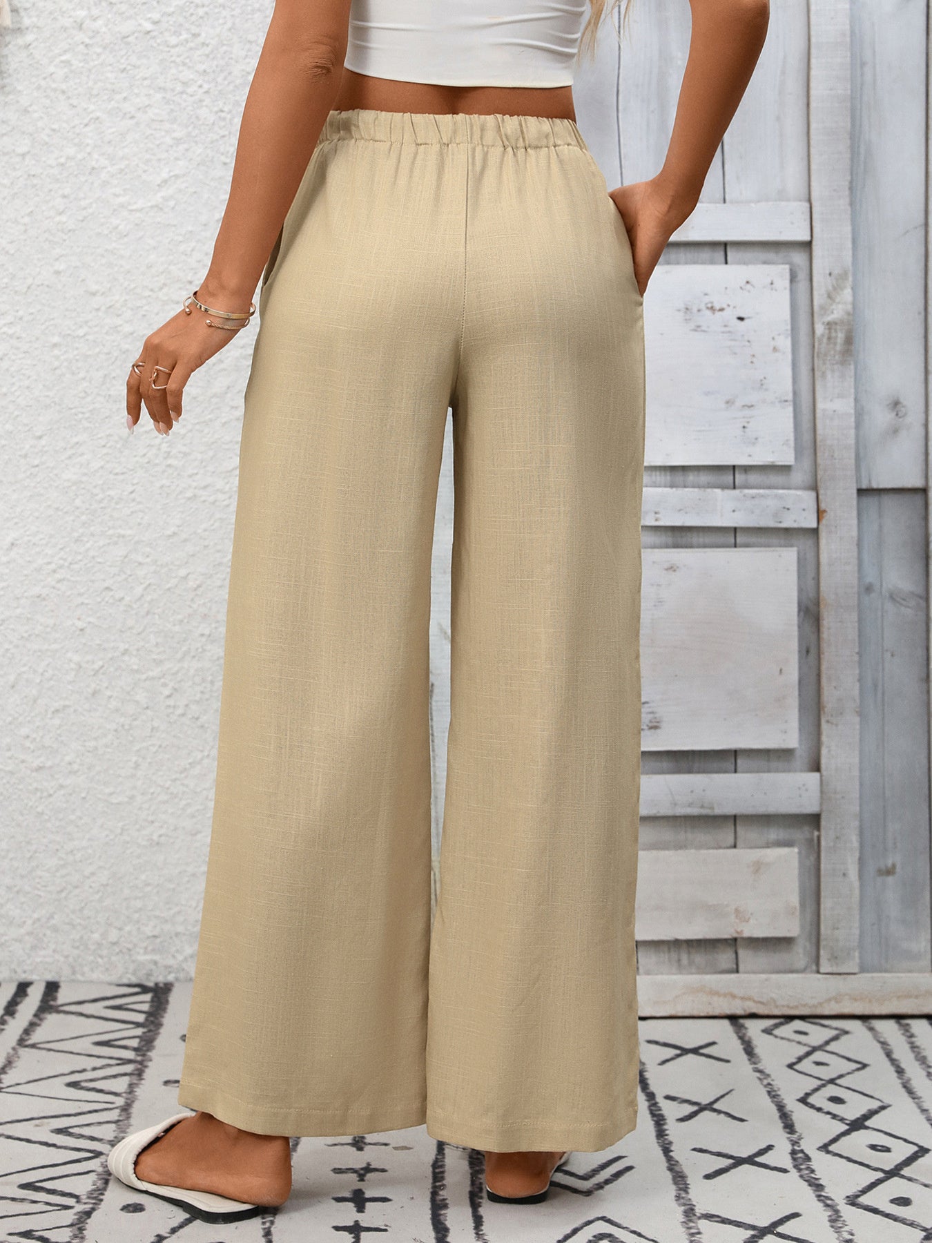 Person wearing beige wide-leg pants with a white top against a light wooden panel background.