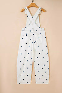 White overalls with black polka dots hanging on a wooden hanger against a beige background