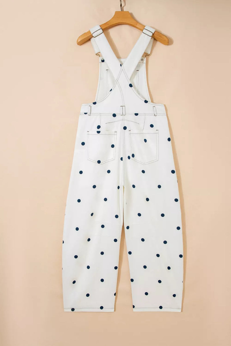 White overalls with black polka dots hanging on a wooden hanger against a beige background