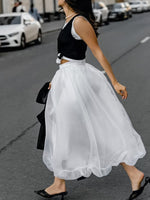 Woman walking on a street wearing a black top and white skirt.