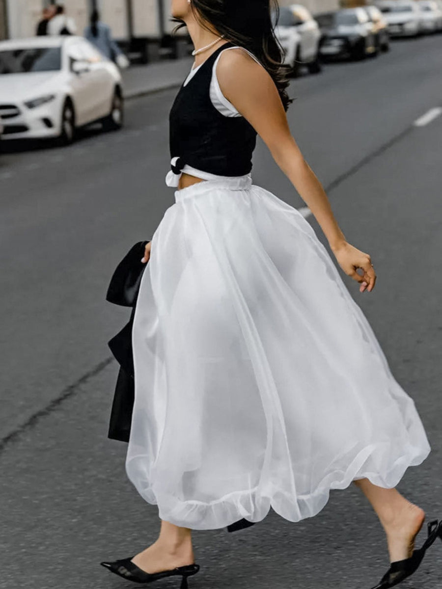 Woman walking on a street wearing a black top and white skirt.