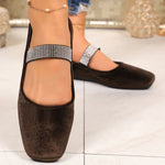 Brown flat shoes with decorative straps worn indoors on a light-colored floor.