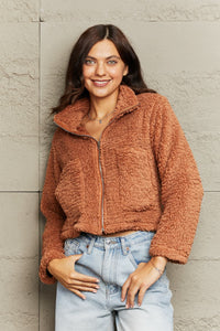Woman wearing a brown fuzzy jacket against a light gray wall