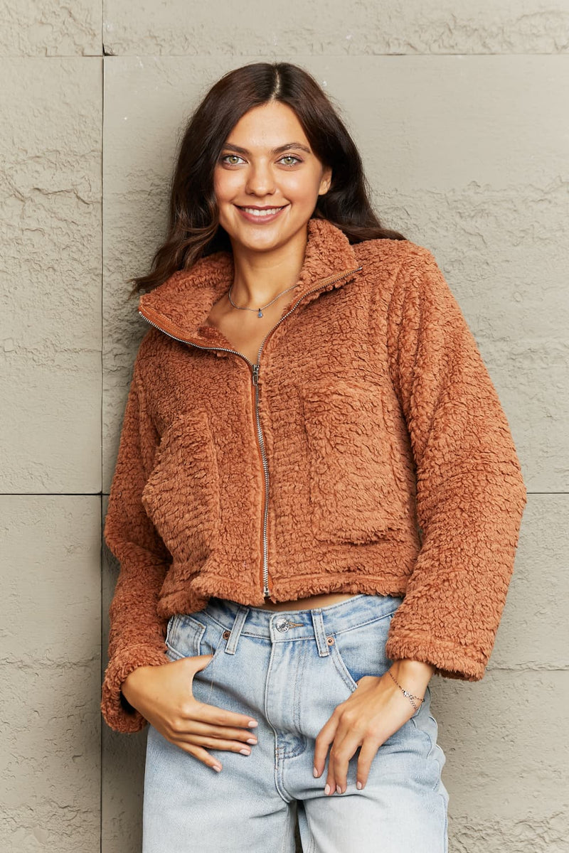 Woman wearing a brown fuzzy jacket against a light gray wall