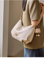 Person holding a white handbag with a bear charm against a neutral background