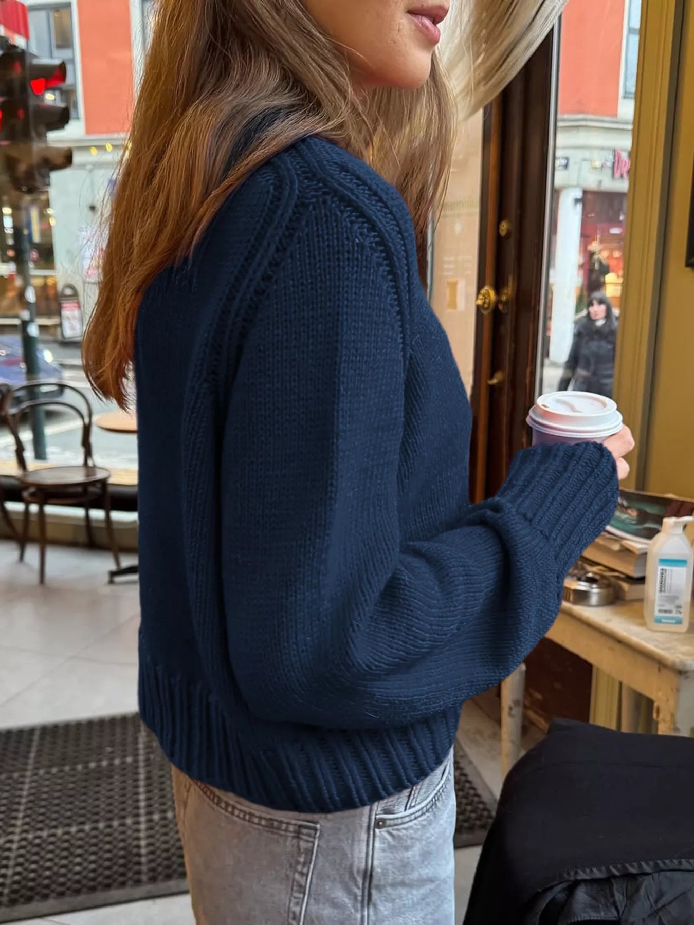 Person wearing a navy blue sweater holding a coffee cup in an indoor setting.