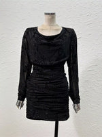 A black long-sleeve mini dress with a cowl neckline and textured ruching, displayed on a mannequin against a white textured wall.