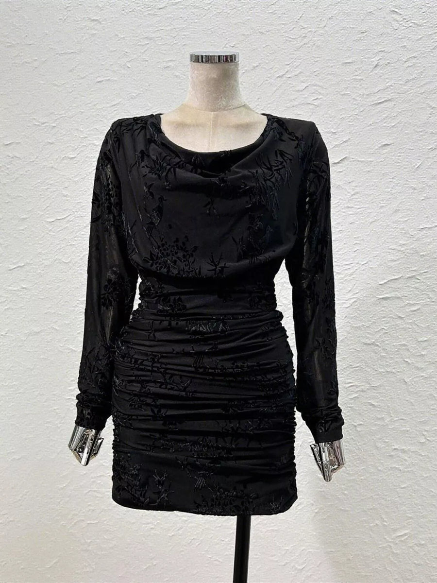 A black long-sleeve mini dress with a cowl neckline and textured ruching, displayed on a mannequin against a white textured wall.
