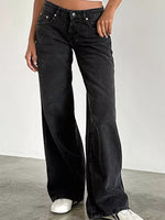 A person wearing black wide-leg denim jeans with a cropped view from the waist down, standing against a plain light gray wall and concrete floor.