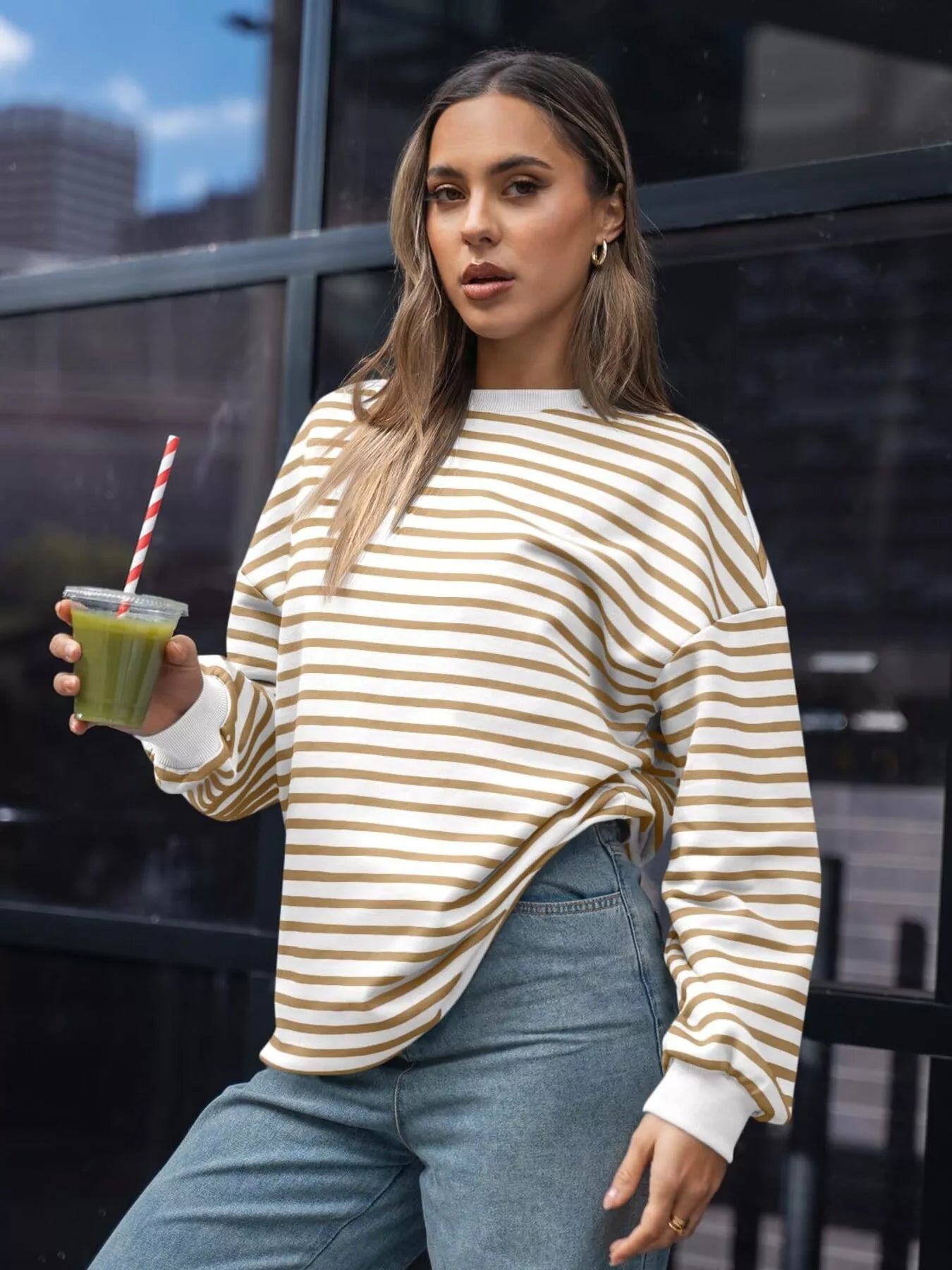 Woman in a striped sweater holding a green smoothie with a straw outdoors.