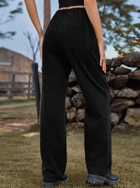 Person wearing black pants standing outdoors with a stone wall and wooden fence in the background