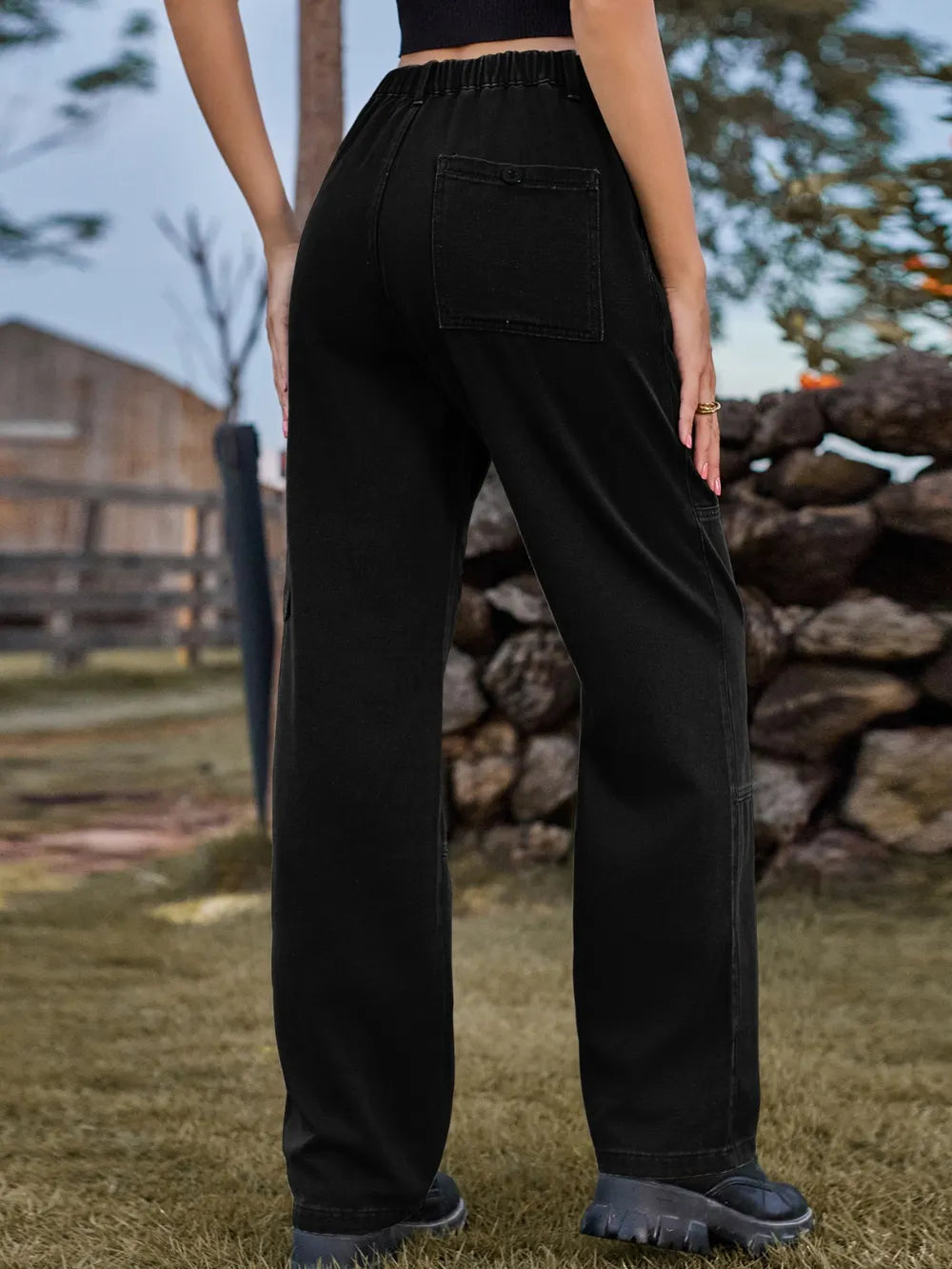Person wearing black pants standing outdoors with a stone wall and wooden fence in the background