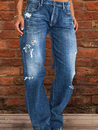 Person wearing distressed blue jeans standing against a brick wall.
