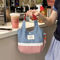 Person holding a small blue and red checkered bag in a cafe setting