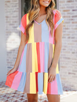 Woman wearing a colorful striped dress against a brick wall.