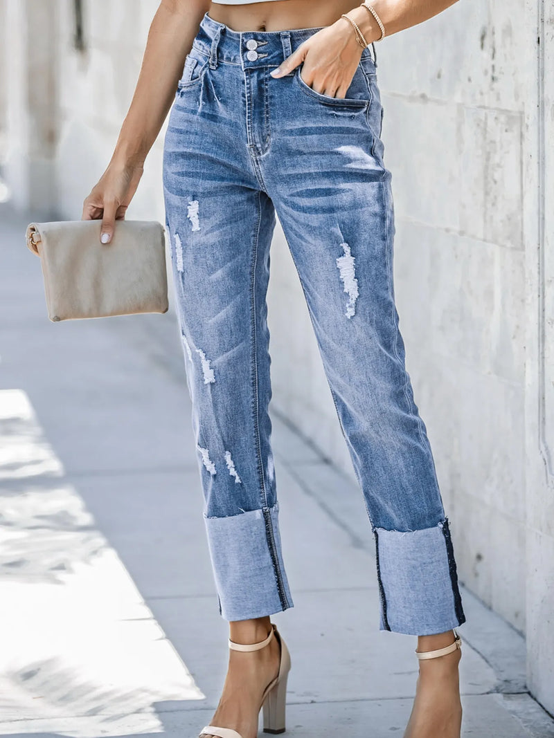 Person wearing distressed blue jeans with a neutral clutch against a light background