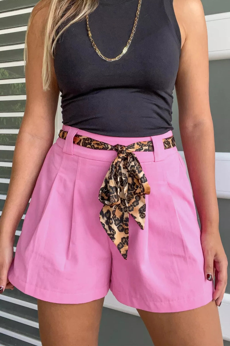 Person wearing a black top and pink shorts with a leopard print belt.