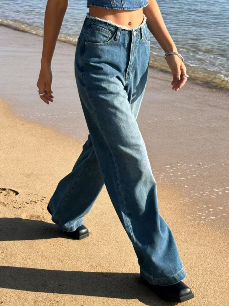 Person wearing blue jeans walking on a sandy beach.