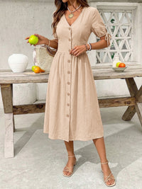 Woman in a beige dress standing in front of a wooden table with fruit.