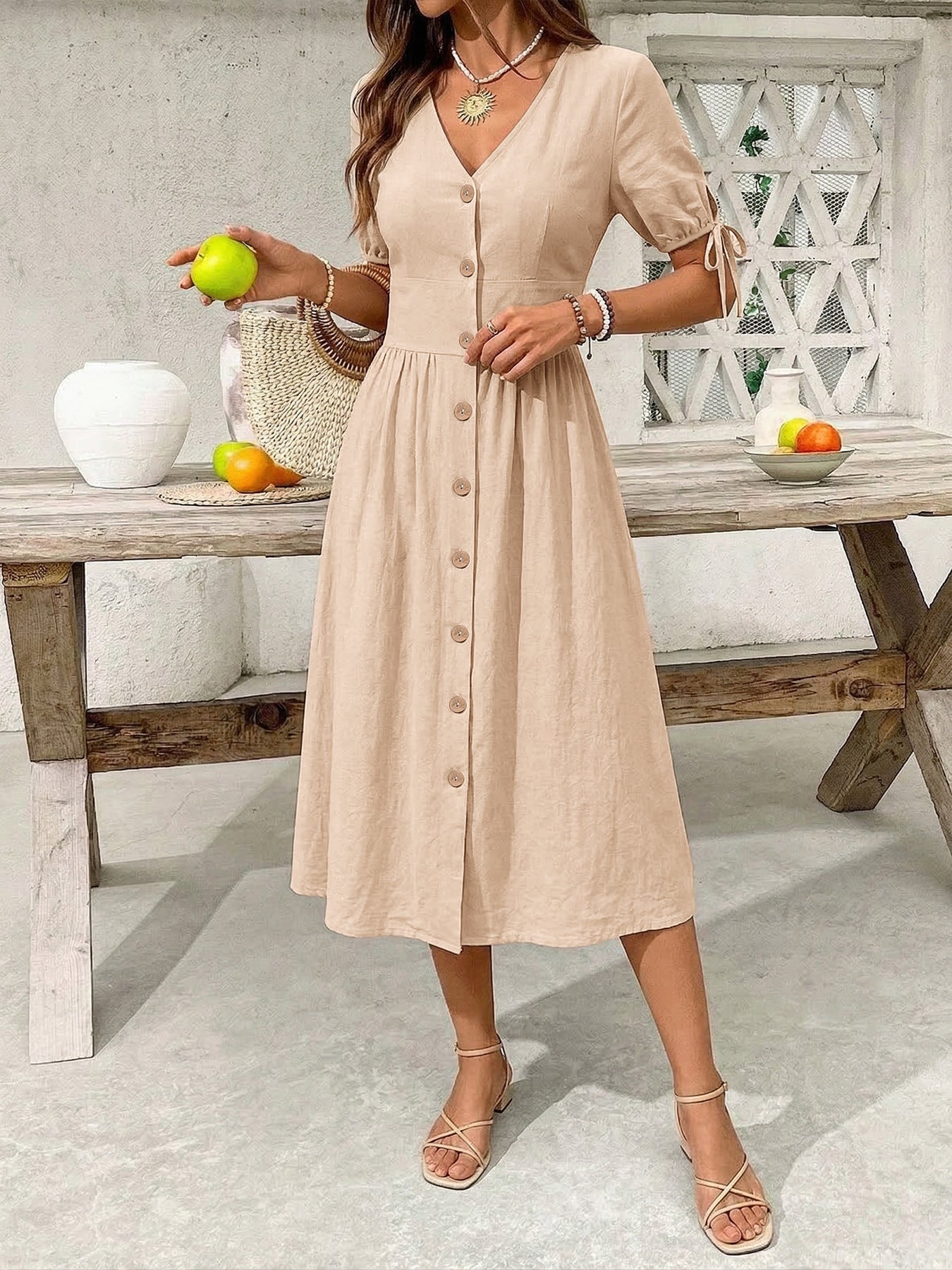 Woman in a beige dress standing in front of a wooden table with fruit.