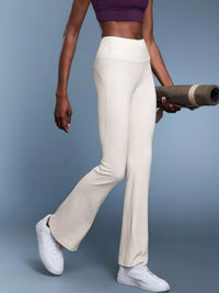Person wearing white pants and a purple top, holding a yoga mat on a blue background