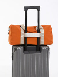 Orange duffel bag with white trim attached to a gray suitcase on a white background
