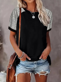 Person wearing a black and gray short-sleeve shirt with denim shorts, holding a brown bag against a gray background.
