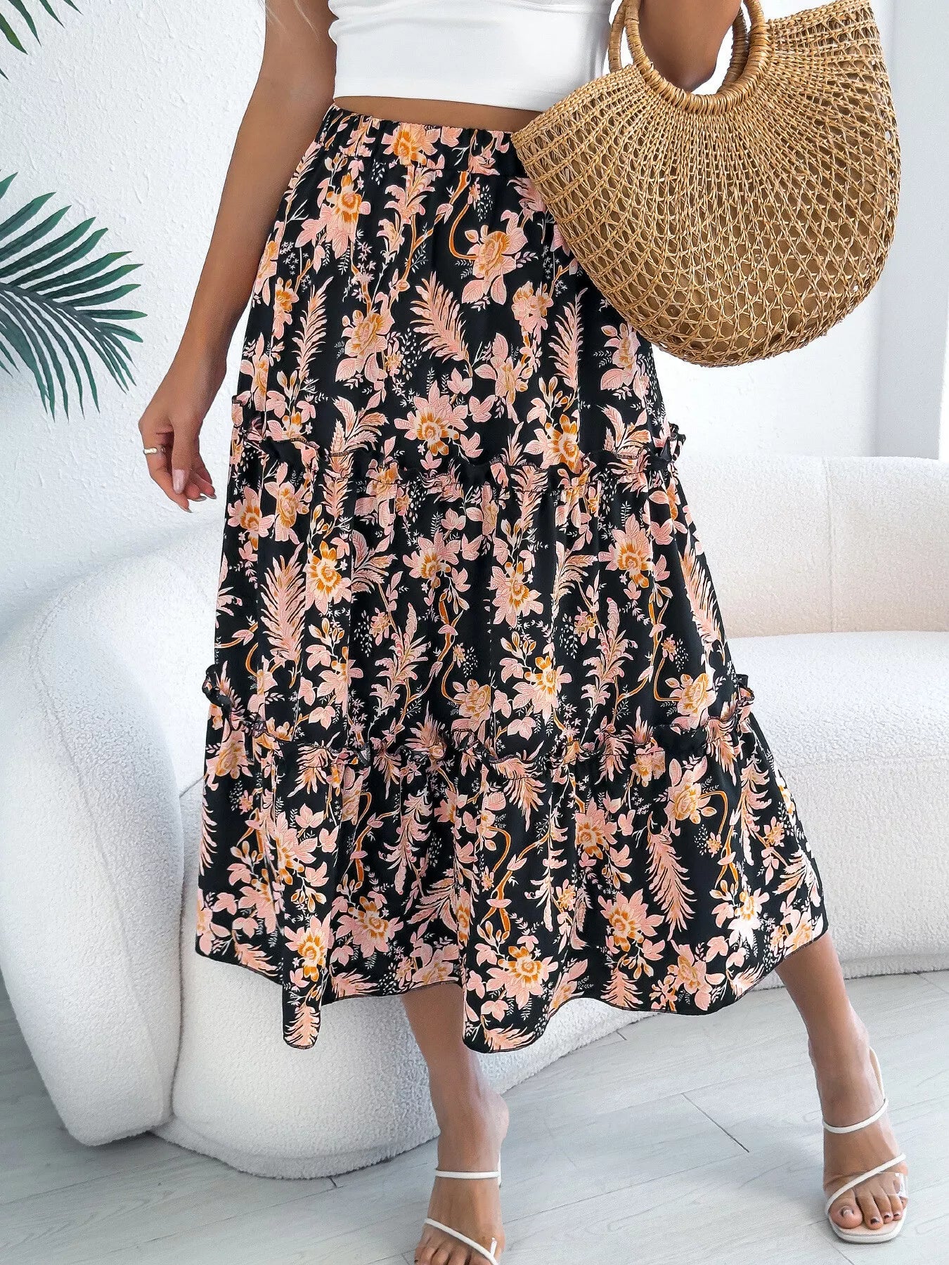 Person wearing a floral skirt with a white top and straw bag indoors.