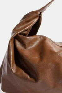 Brown leather handbag with a visible tear on a white background