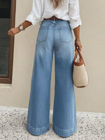 Person wearing blue wide-leg jeans and a white shirt, holding a woven handbag.