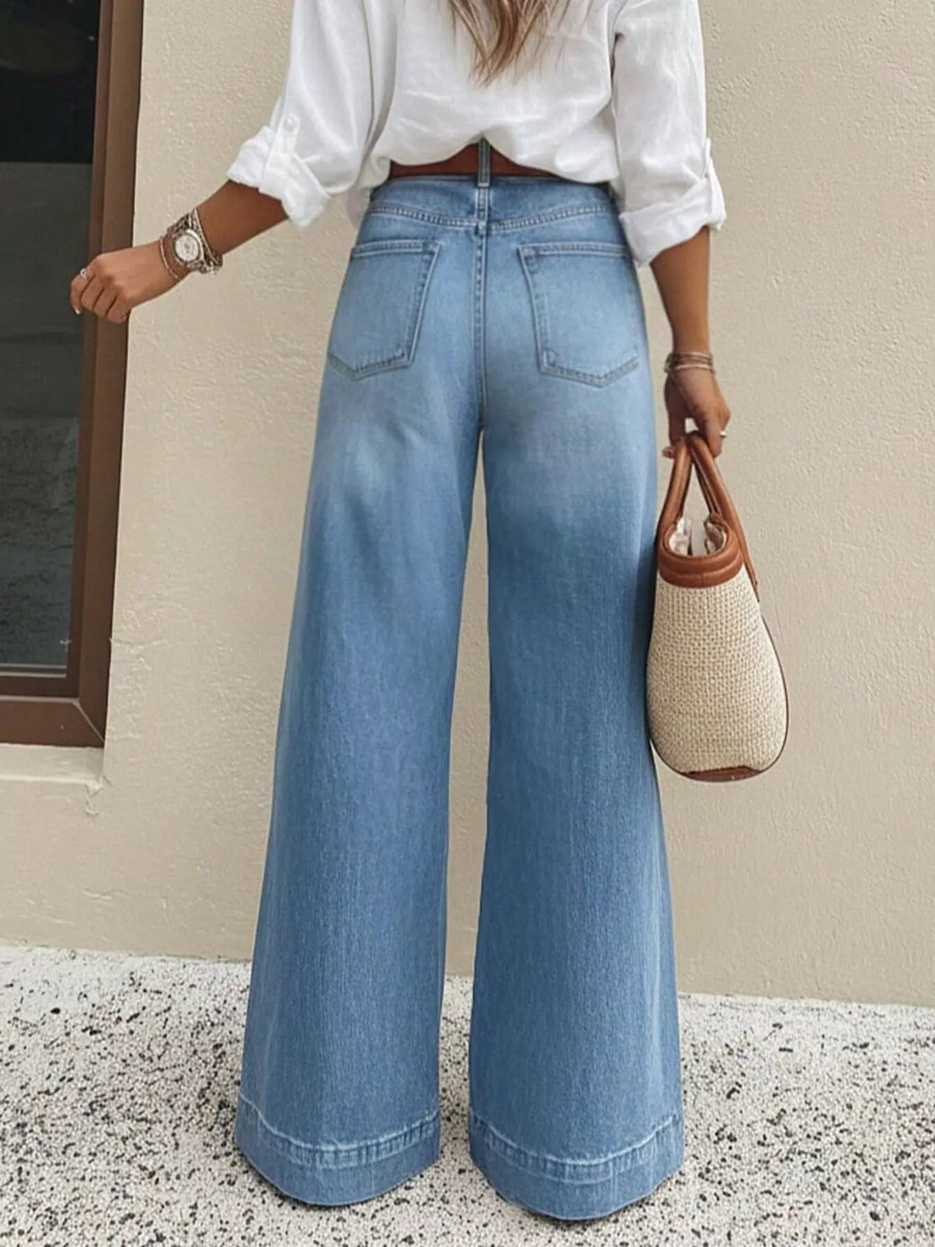 Person wearing blue wide-leg jeans and a white shirt, holding a woven handbag.