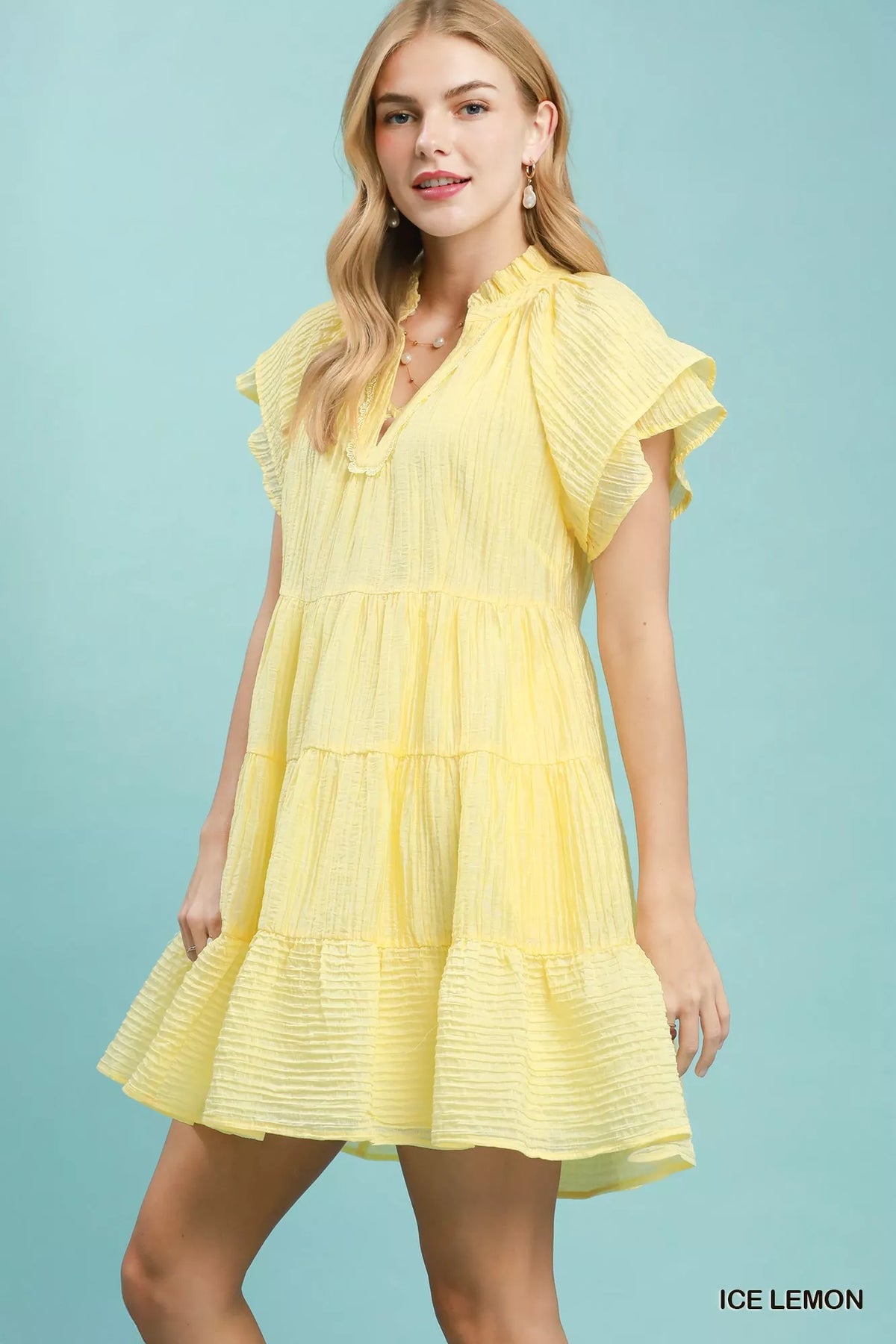 Woman wearing a yellow dress with ruffled sleeves against a light blue background