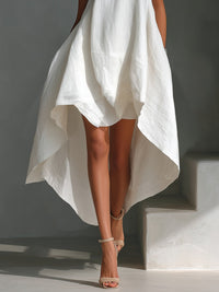 White dress with an asymmetrical hemline worn by a person on a gray background