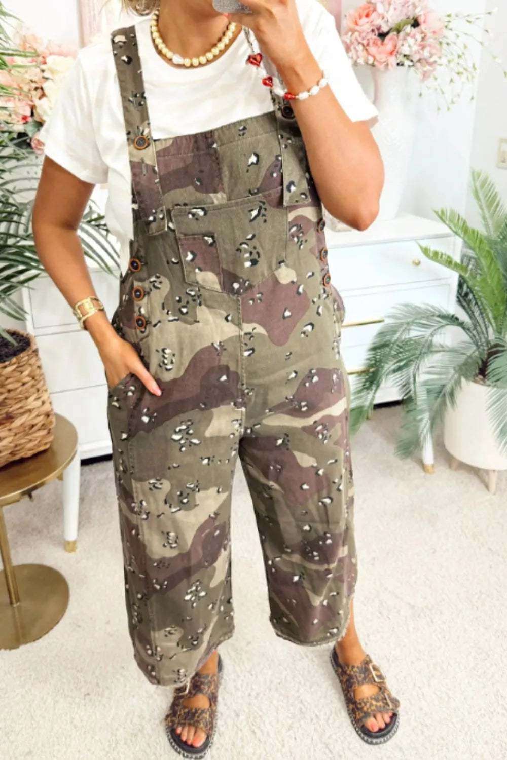 Person wearing camouflage overalls in a home setting with plants and furniture.