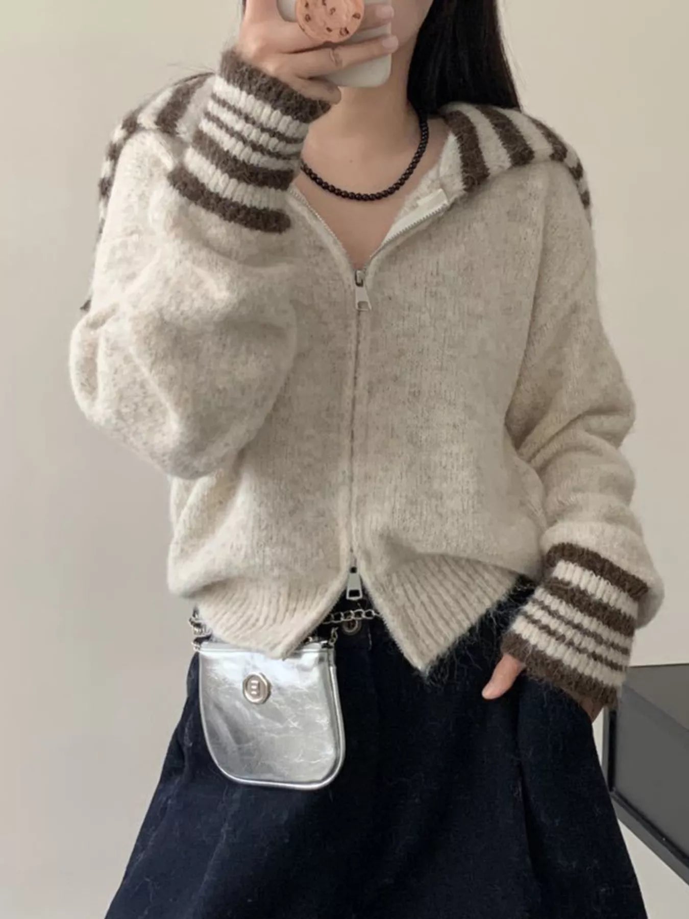 Person wearing a beige and brown striped sweater with a silver bag.
