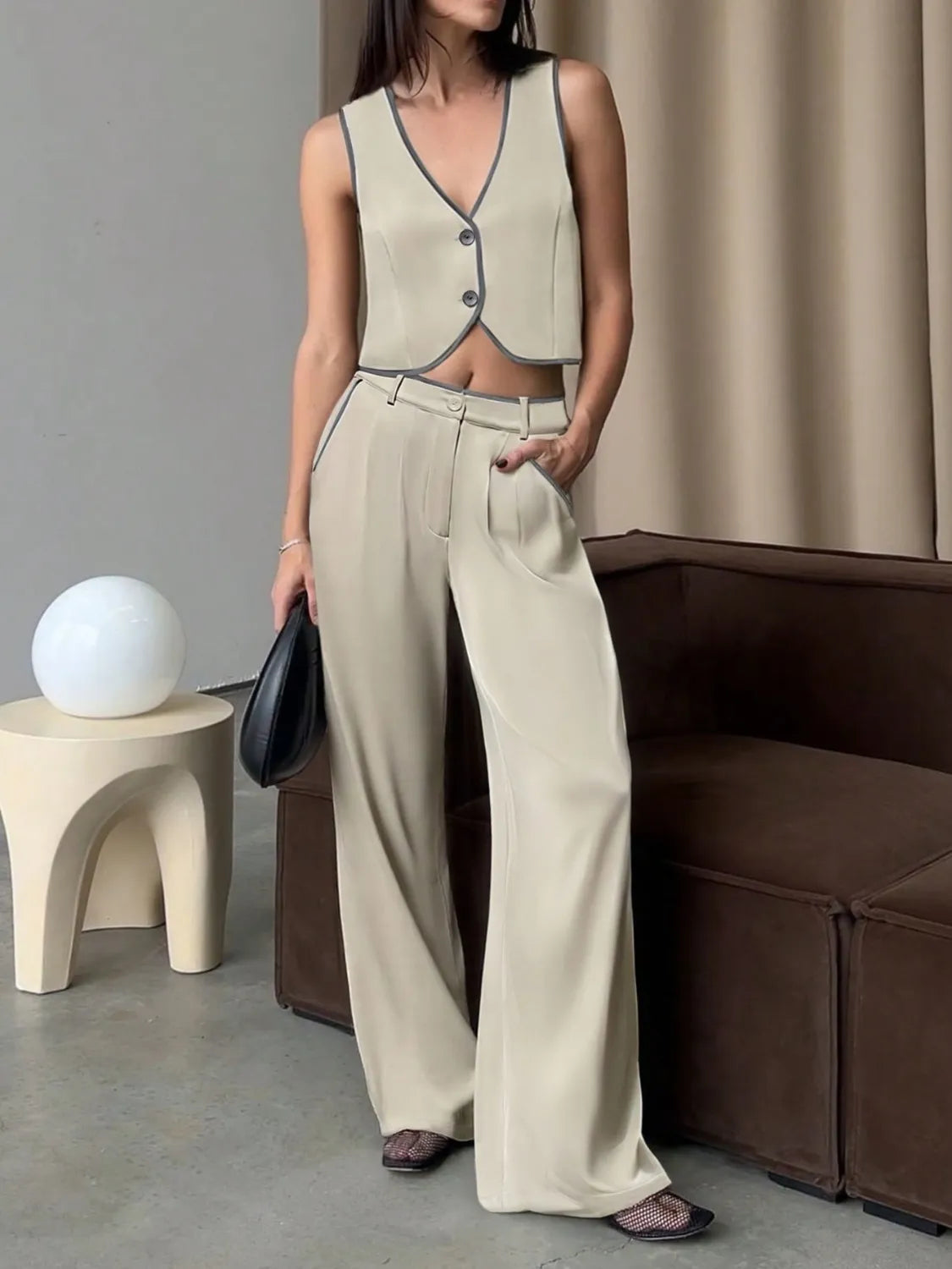 Woman in beige sleeveless top and wide-leg pants standing in a modern interior setting.