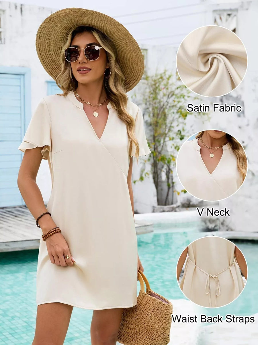 Woman wearing a cream-colored dress with details highlighted, standing by a pool.