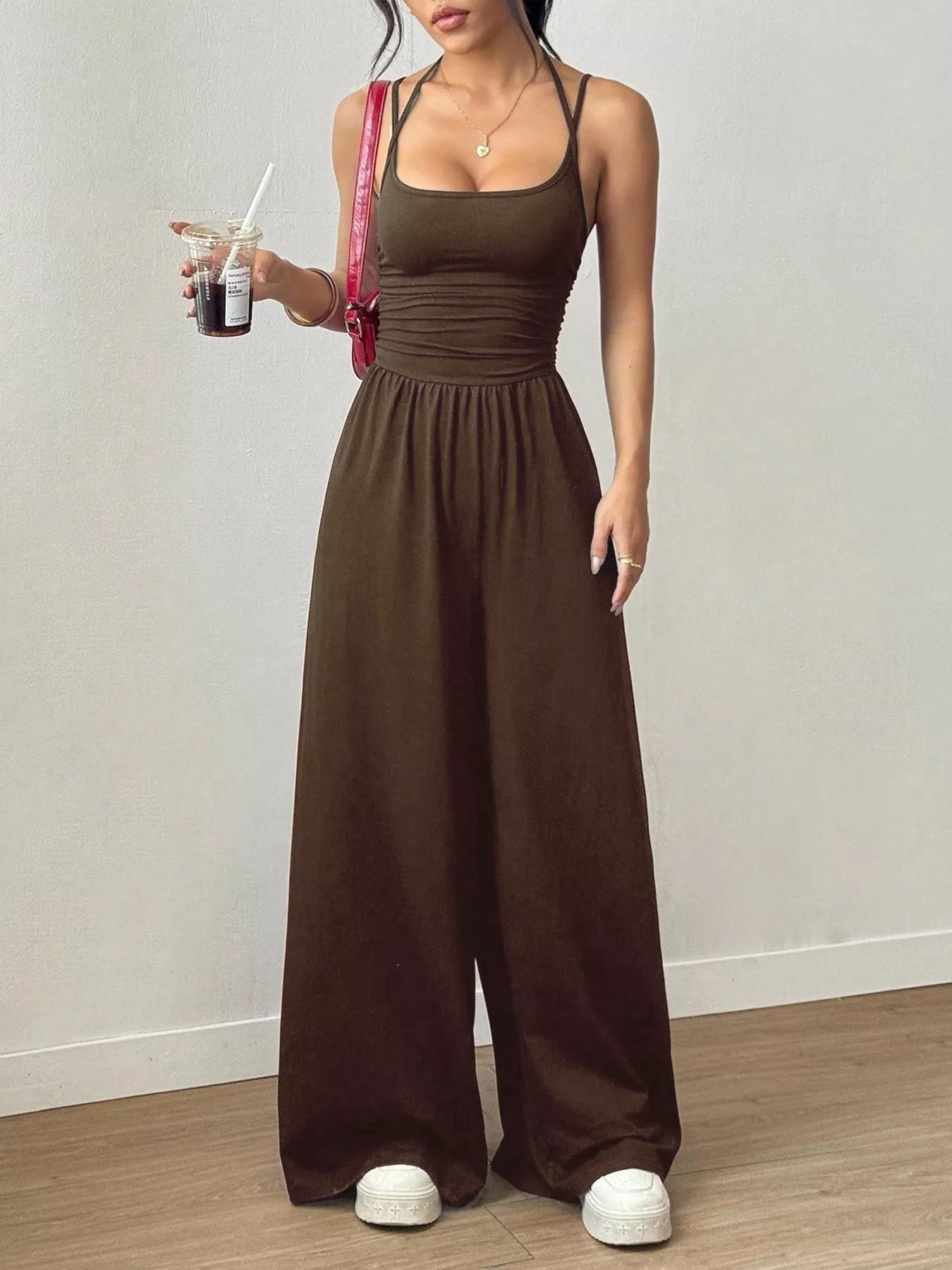 Woman wearing a brown jumpsuit holding a drink against a plain background