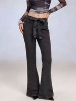Person wearing a long-sleeve crop top and black flared jeans on a plain background