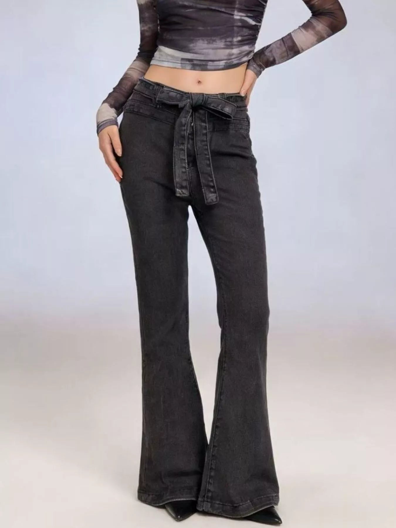 Person wearing a long-sleeve crop top and black flared jeans on a plain background